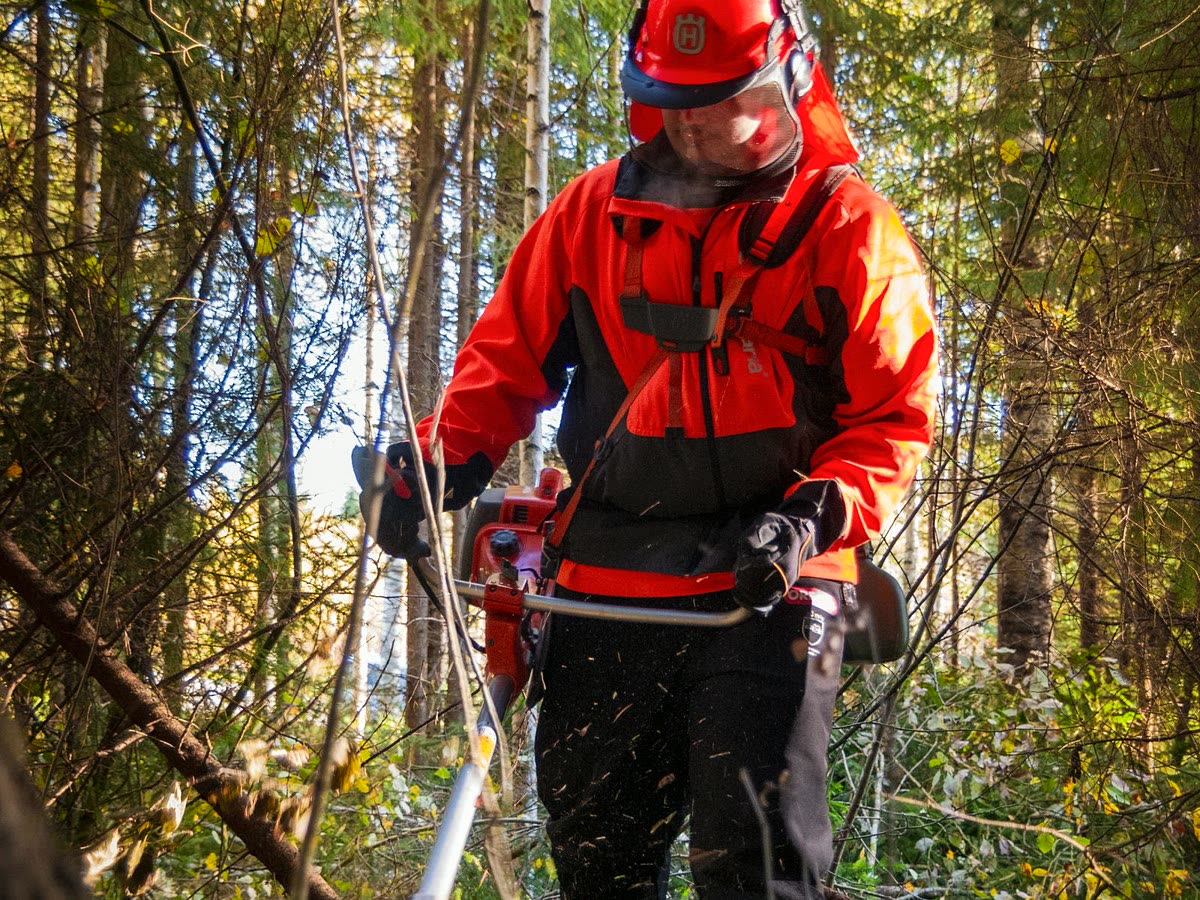 Operative in full protective equipment clearing scrub with a brush cutter