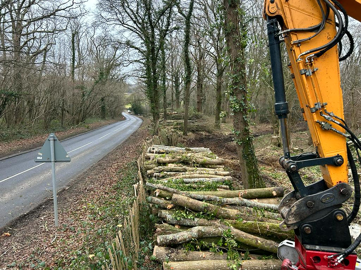 Roadside vegetation cleared and timber stacked with an excavator on a country road